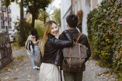 Rear view of man walking with female friend looking over shoulder on sidewalk