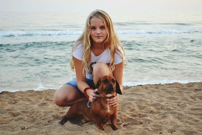 Portrait of girl crouching with dog at beach