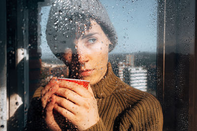 Portrait of woman looking through wet window