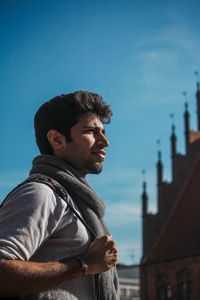 Side view of young man looking away against blue sky