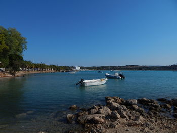 Boats in calm sea against clear sky