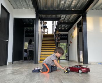 Side view of boy kid playing on the floor with car toy red color. house stairs behind 