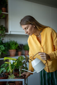 Female growing houseplants at home checking soil dryness, watering potted houseplants with water can