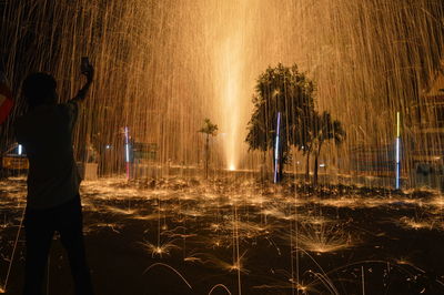 Rear view of man standing by illuminated fountain at night