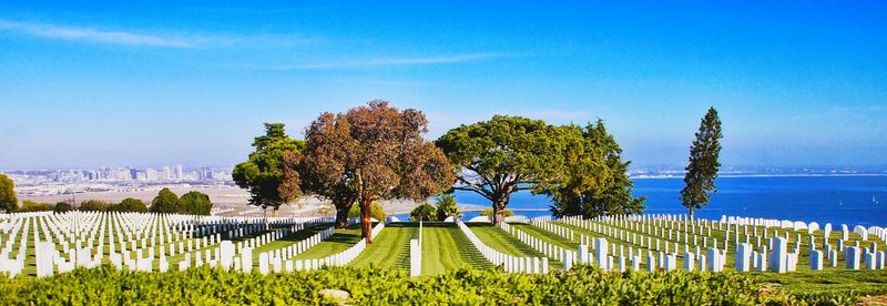 Panoramic view of tombstones by sea against blue sky at cemetery