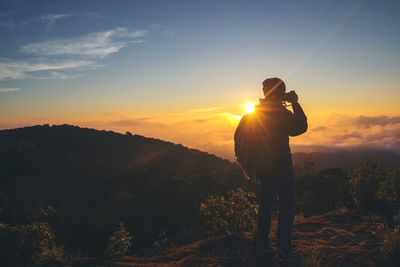 Man photographing on mountain against sky at sunset