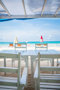 Empty table and chairs at shore of beach against sky