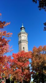 Low angle view of trees and lighthouse against clear blue sky