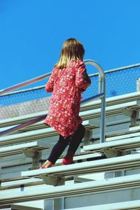 Rear view of girl walking on stairs against clear blue sky