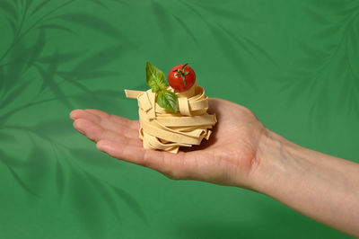 Pasta tagliatelle nest in hand isolated on a green background