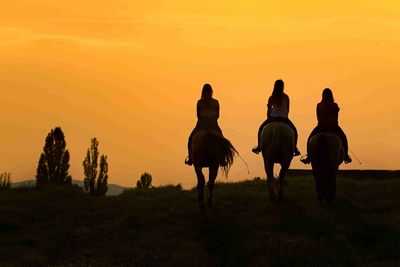 Rear view of girls riding horse on field against sky at dusk