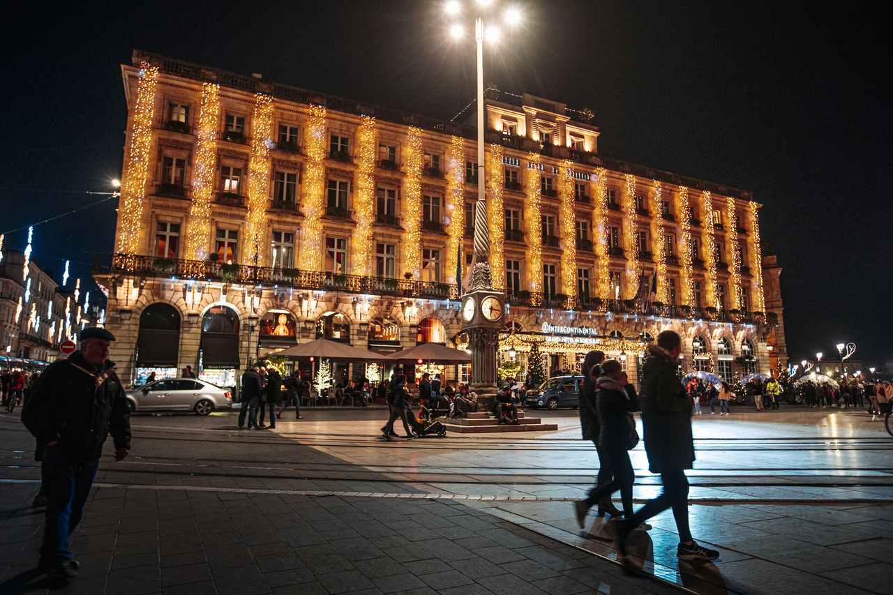 PEOPLE WALKING ON ILLUMINATED STREET IN CITY