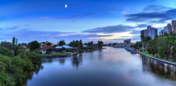 Scenic view of river by buildings against sky at dusk