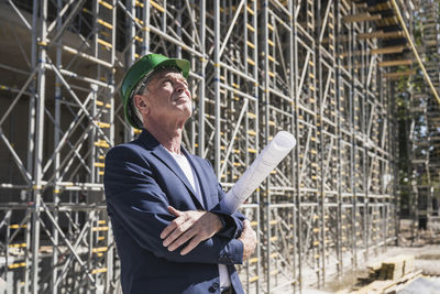 Thoughtful architect with blueprint at construction site