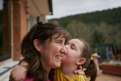Side view of cheerful woman hugging daughter while resting on bench
