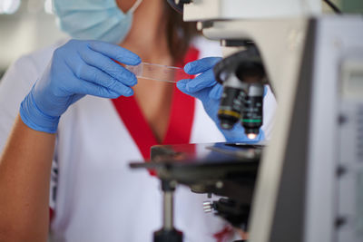 Crop unrecognizable female specialist in uniform with medical sample near microscope at work in laboratory