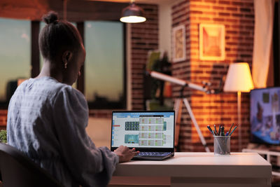 Rear view of woman using digital tablet while sitting in cafe