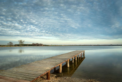 Long wooden bridge towards the lake and evening clouds on the sky