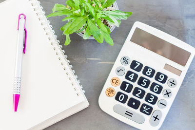 High angle view of calculator with pen and spiral notebook on table