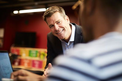 Smiling bank manager looking at male entrepreneur giving presentation in creative office