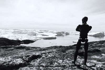 Man standing on rock by sea against sky