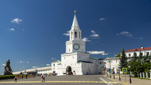 People on street amidst buildings against blue sky