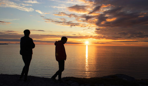 Silhouette people standing on beach against sky during sunset