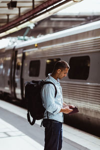 Mid adult man with backpack using mobile phone while standing by train on platform