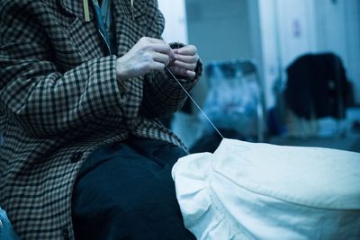 Midsection of woman sewing fabric while sitting in workshop