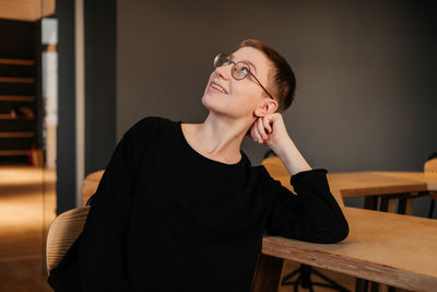 Young woman with short hair in eyeglasses and black sweater sitting at the table in office