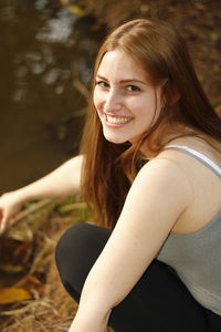 High angle portrait of beautiful woman crouching at lakeshore in park