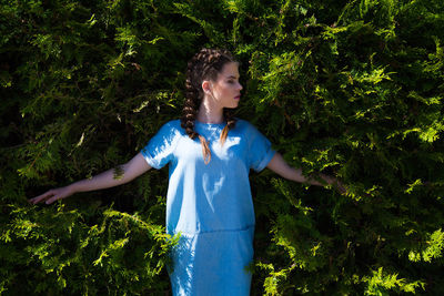 Young woman standing by tree against plants