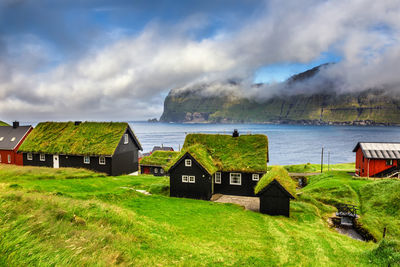 Houses on field by sea against sky