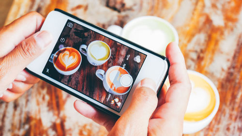 Cropped hands photographing coffee cups with mobile phone in cafe