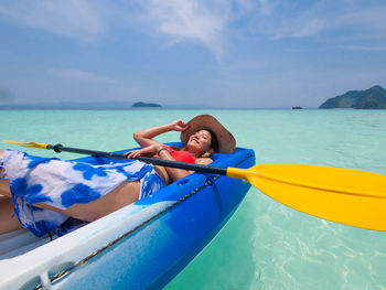 Young woman lying in boat on sea against sky