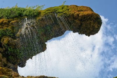 Low angle view of water falling from cliff against sky