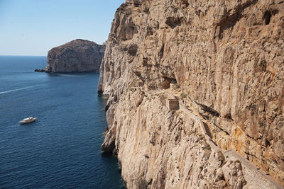 Stairway in limestone rock to stalactite neptune cave. boat leaving grotte di nettuno.sardinia,italy