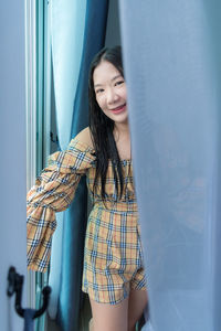 Young woman smiling while standing against curtain