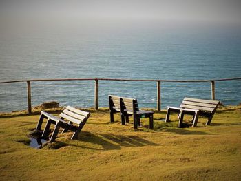 Empty benches on shore by ocean against sky