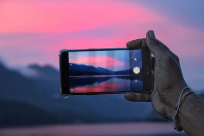 Man photographing with mobile phone against sky