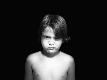 Portrait of shirtless boy sulking against black background