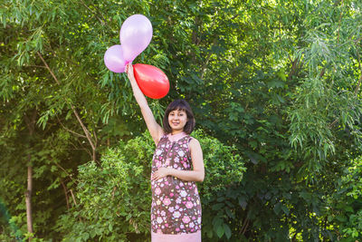 Full length of woman with pink balloons standing against plants