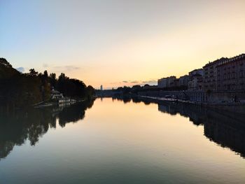 River amidst buildings against sky during sunset