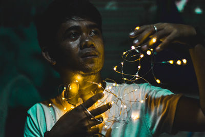 Close-up of man holding illuminated string lights