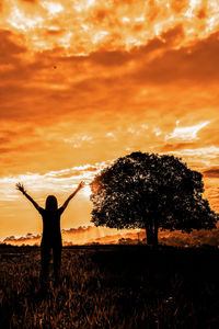 Rear view of silhouette person standing on field against sky during sunset