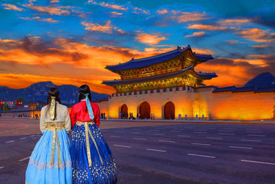 Rear view of people standing at temple during sunset