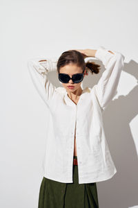 Young woman wearing sunglasses while standing against white background