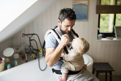 Father with baby in baby carrier brushing his teeth