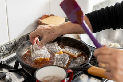 Close up of old lady's hand placing cod into a frying pan.