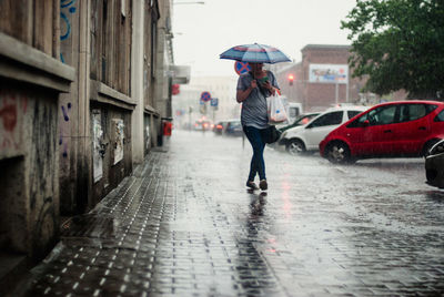 Woman holding umbrella while walking on sidewalk during rainy season